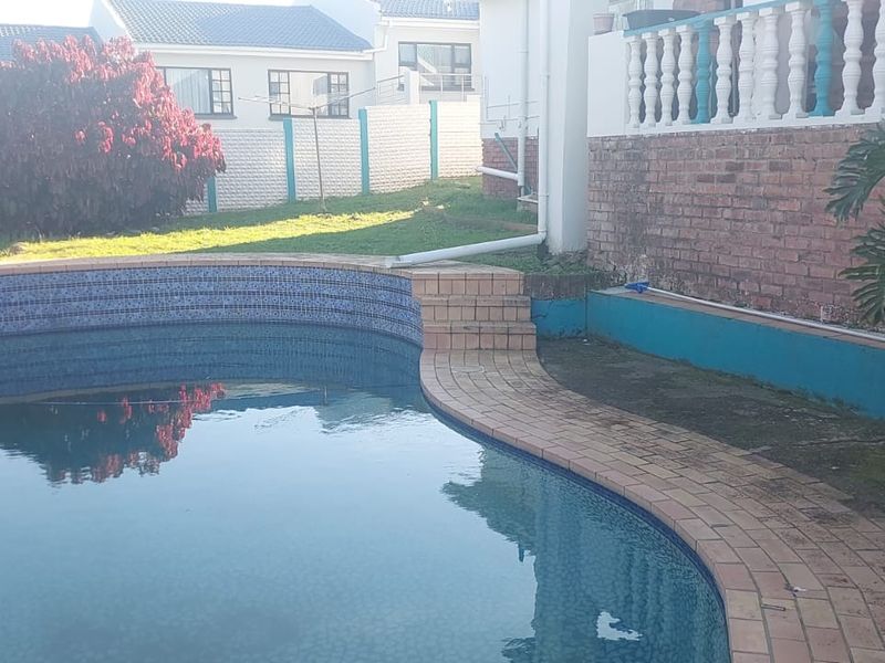 Outdoor pool area featuring a curved swimming pool with brick paving, a brick retaining wall, and a white balustrade on the upper level.