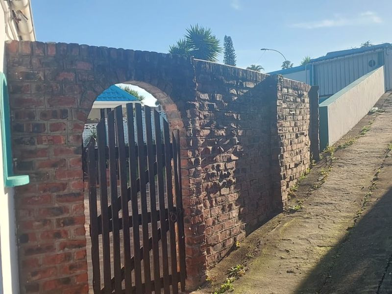 A view of the property entrance featuring a brick boundary wall with an arched gate and a concrete driveway leading up to the residence.