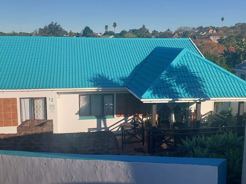 Front view of a residential property featuring a distinctive bright blue metal roof, covered patio area, and a brick boundary wall.