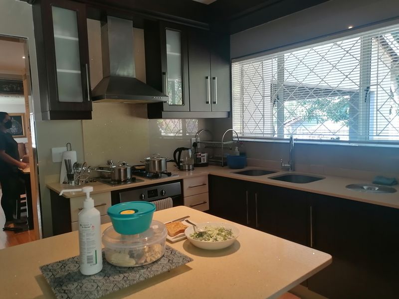 A functional kitchen featuring dark cabinetry, stone countertops, a gas hob with extractor fan, and a double sink with window views.