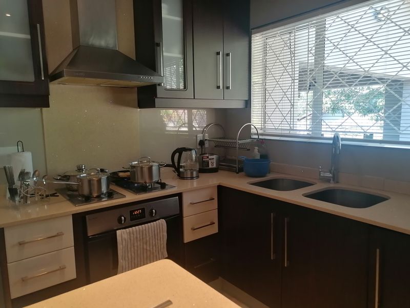 A functional kitchen featuring dark cabinetry, stone countertops, a built-in oven with gas hob, and a double basin sink with a window view.