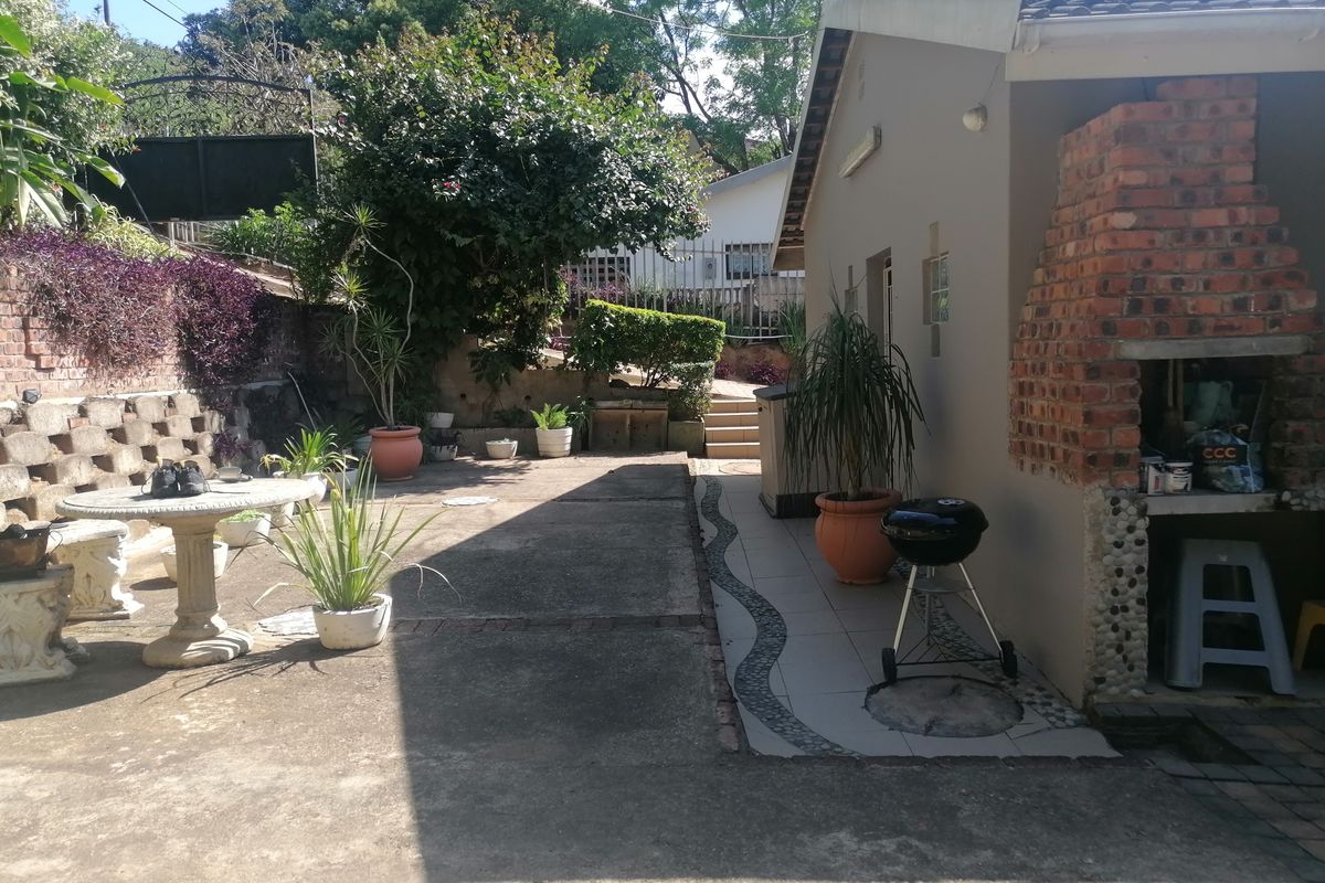 Rear exterior area featuring a concrete patio, a built-in brick braai, and a tiered garden with a retaining wall.