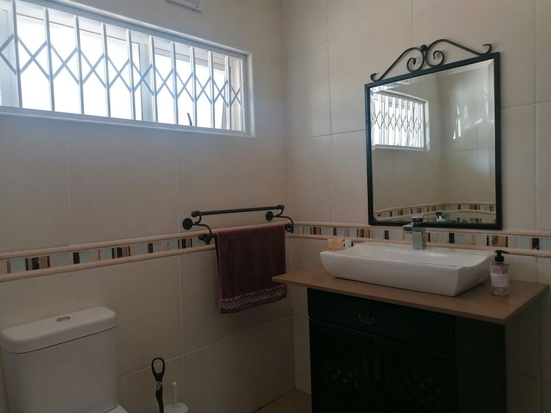 A functional bathroom featuring a modern vessel sink on a vanity cabinet, tiled walls, and a window fitted with a security gate.