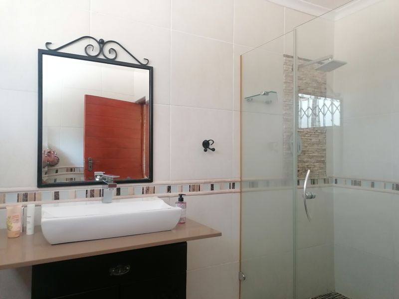 Modern bathroom featuring a vessel sink on a vanity cabinet, a glass-enclosed shower with a rain shower head, and decorative mosaic tile accents.
