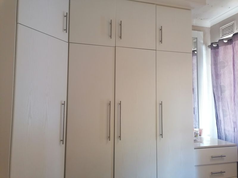 Bedroom featuring floor-to-ceiling built-in cupboards with modern handles and a window with natural light.