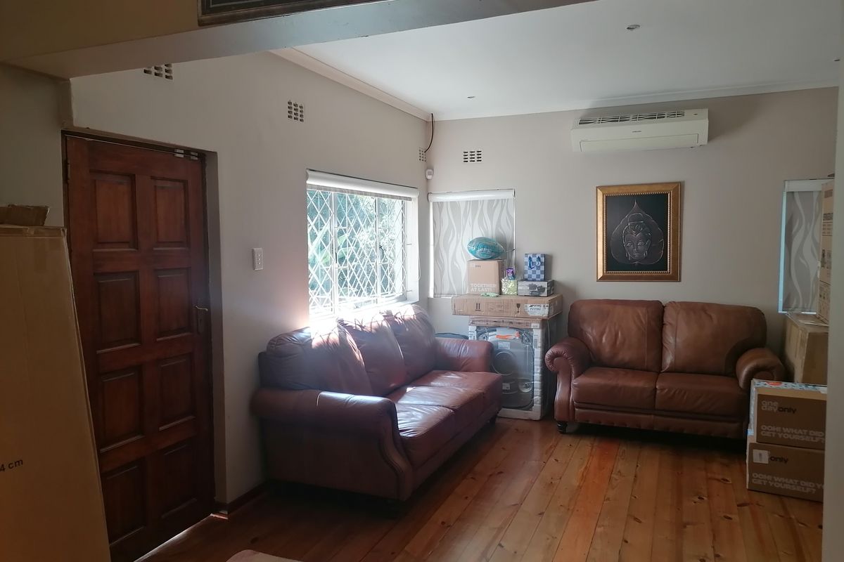 A living room featuring polished timber flooring, a wall-mounted air conditioning unit, and security-barred windows, providing a functional and well-lit living space.