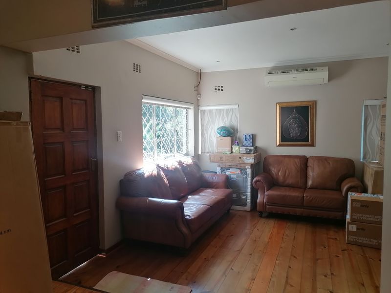 A living room featuring polished timber flooring, a wall-mounted air conditioning unit, and security-barred windows, providing a functional and well-lit living space.