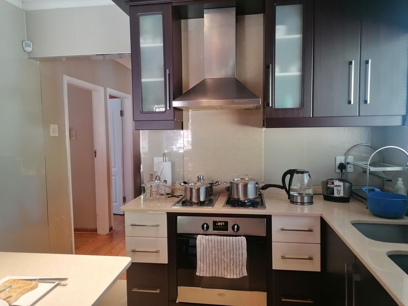 A functional kitchen featuring dark wood cabinetry, stone countertops, a stainless steel oven and hob, and a tiled splashback.