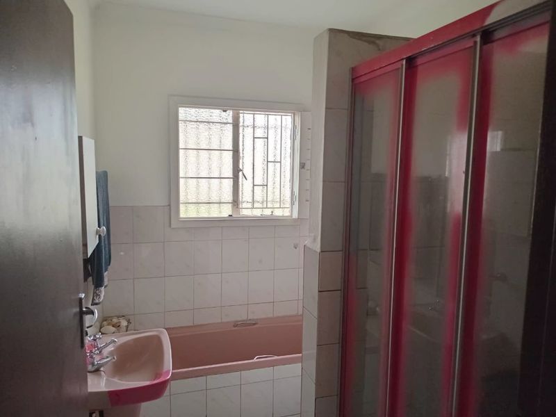 A dated bathroom featuring a pink pedestal basin and bathtub, with a separate shower enclosure and security bars on the window.