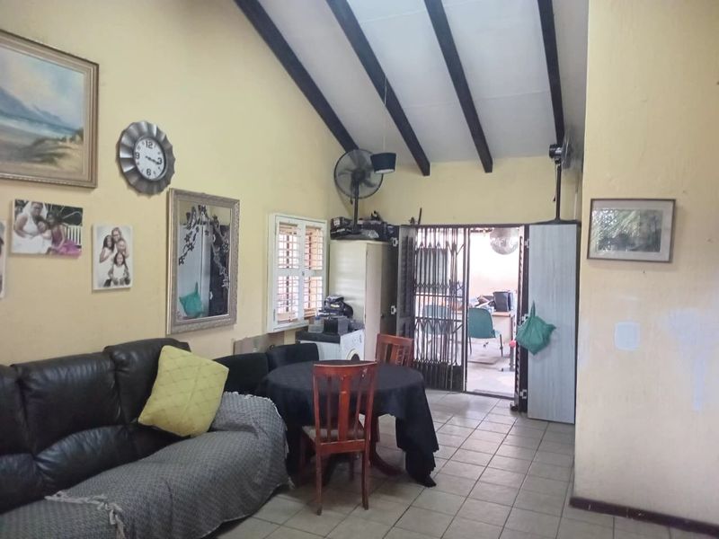 Open plan living area featuring exposed timber ceiling beams, tiled flooring, and direct access to an outdoor patio through a security gate.