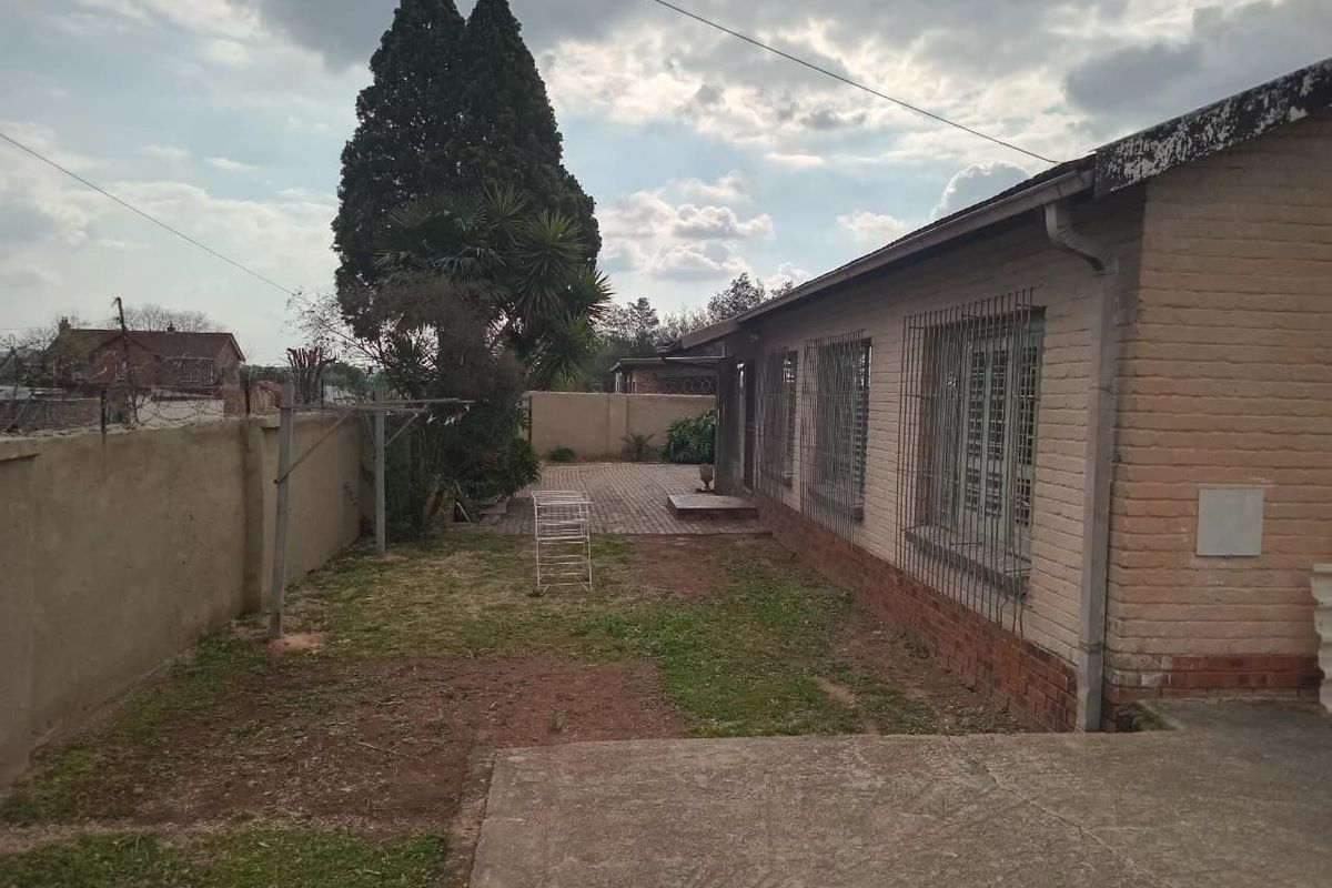 Rear exterior view of the property featuring a brick facade, security bars on windows, a paved patio area, and a fenced garden space.