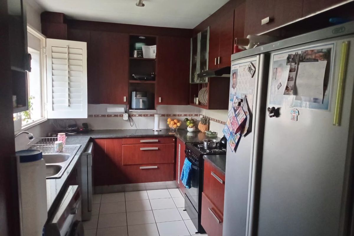 A functional kitchen featuring dark wood cabinetry, granite countertops, tiled flooring, and integrated gas stove with extractor fan.