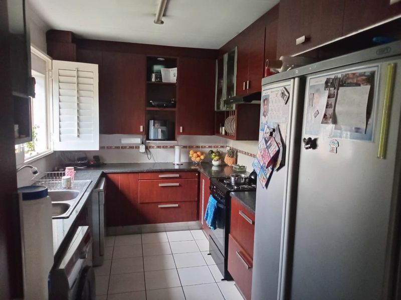 A functional kitchen featuring dark wood cabinetry, granite countertops, tiled flooring, and integrated gas stove with extractor fan.