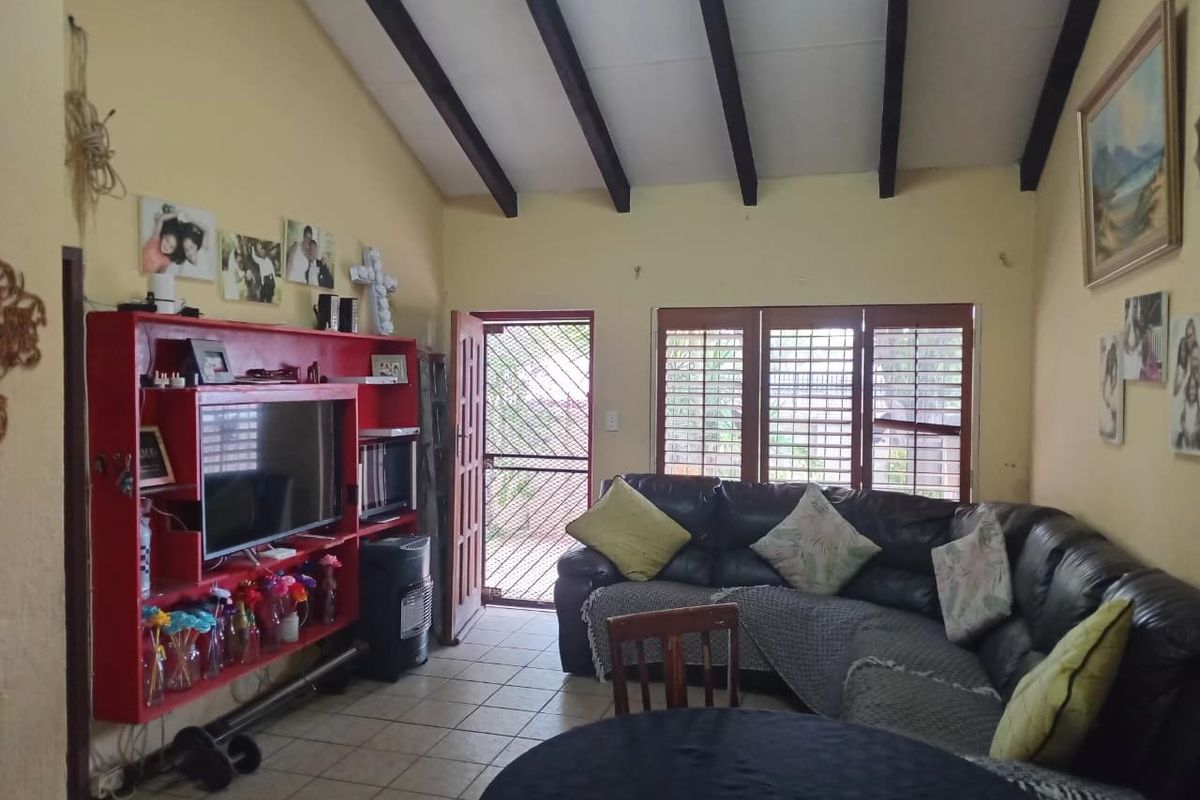 Living room featuring exposed timber ceiling beams, tiled flooring, and security shutters, offering a functional space with potential for cosmetic updates.