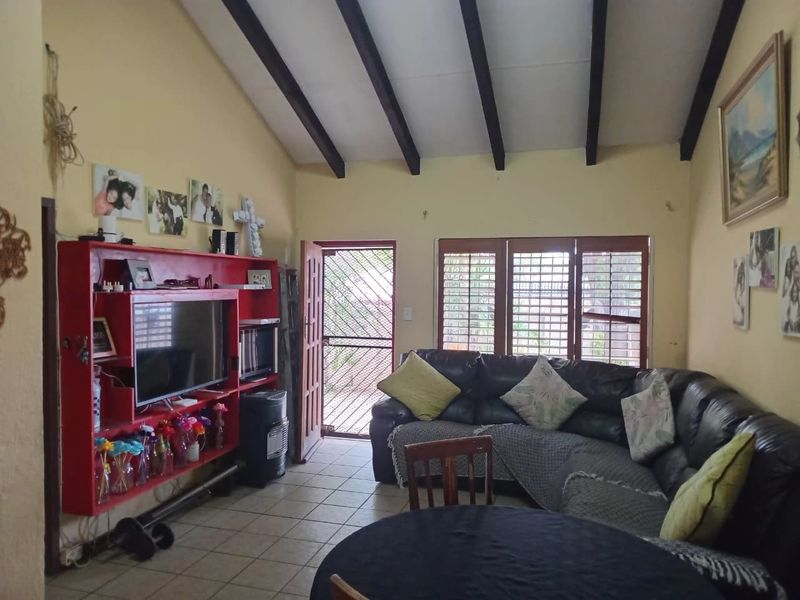Living room featuring exposed timber ceiling beams, tiled flooring, and security shutters, offering a functional space with potential for cosmetic updates.