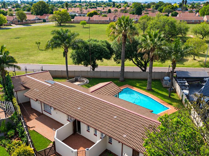 Aerial view of a residential property featuring a swimming pool, tiled roof, and a spacious garden area within a secure perimeter.
