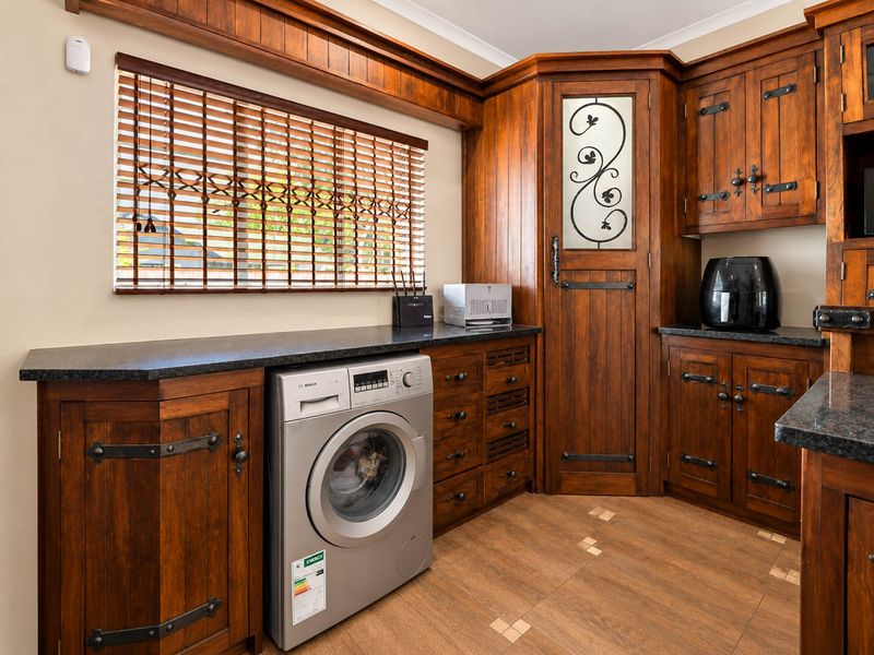A well-maintained laundry room featuring custom dark wood cabinetry, stone countertops, and integrated washing machine with tiled flooring and wooden blinds.