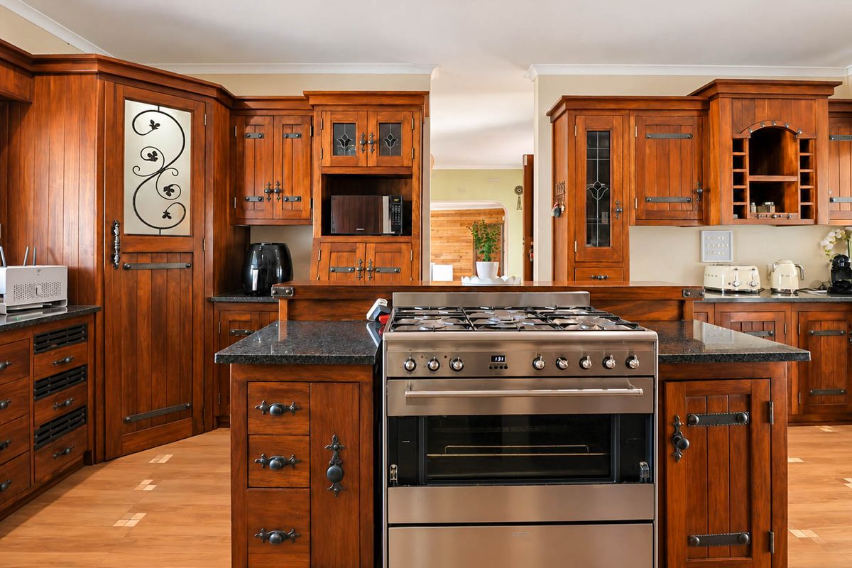 A traditional kitchen featuring warm-toned wooden cabinetry, granite countertops, and a central island with a stainless steel gas stove and oven.