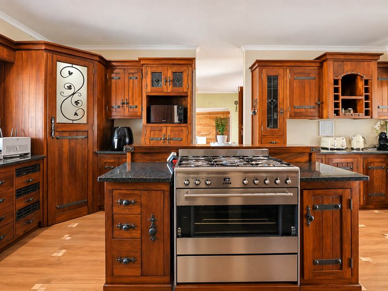 A traditional kitchen featuring warm-toned wooden cabinetry, granite countertops, and a central island with a stainless steel gas stove and oven.