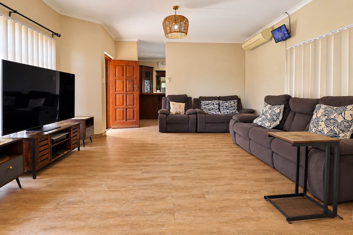 Spacious living room featuring wood-look tile flooring, neutral walls, and a wall-mounted air conditioning unit.
