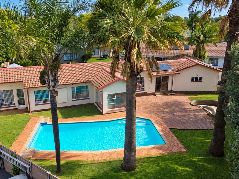 Aerial view of the property featuring a swimming pool, paved patio area, and a tiled roof with installed solar panels.