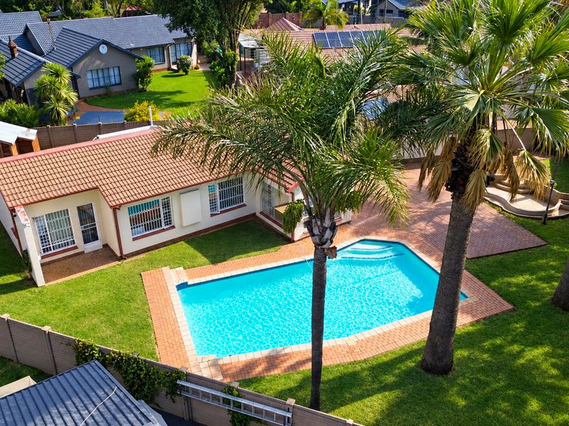 Aerial view of the property featuring a swimming pool, paved patio area, landscaped garden, and secure boundary walls.