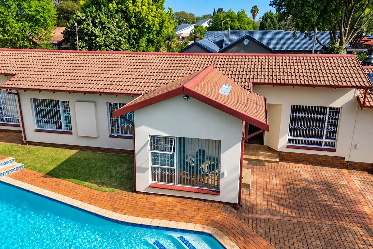 Aerial view of the rear exterior featuring a swimming pool, paved patio area, and a well-maintained house with terracotta roof tiles and security bars.