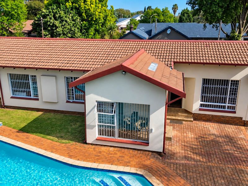 Aerial view of the rear exterior featuring a swimming pool, paved patio area, and a well-maintained house with terracotta roof tiles and security bars.