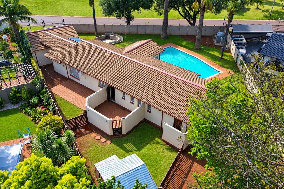Aerial view of a residential property featuring a tiled roof house, a swimming pool, paved patio areas, and a well-maintained garden.