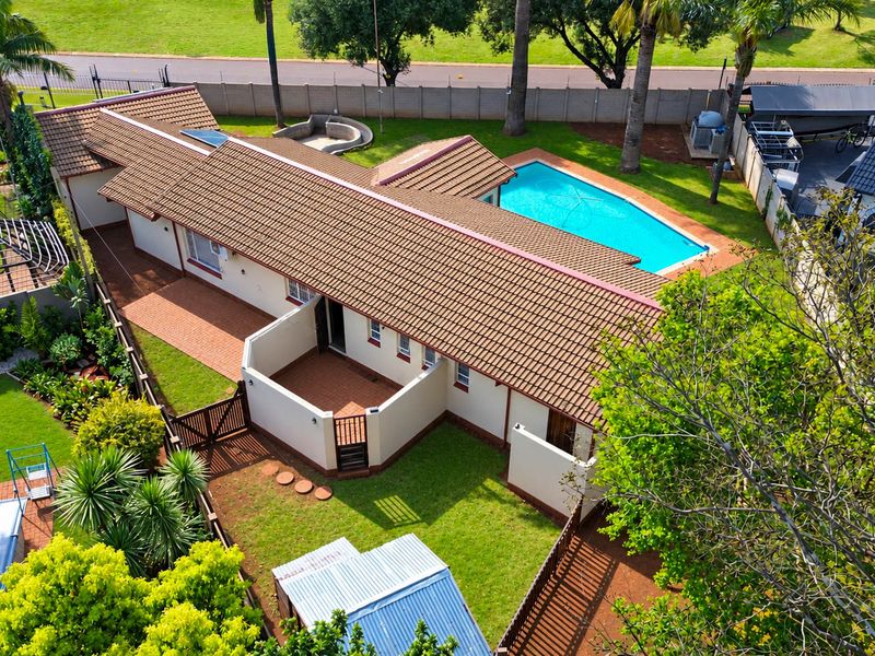 Aerial view of a residential property featuring a tiled roof house, a swimming pool, paved patio areas, and a well-maintained garden.