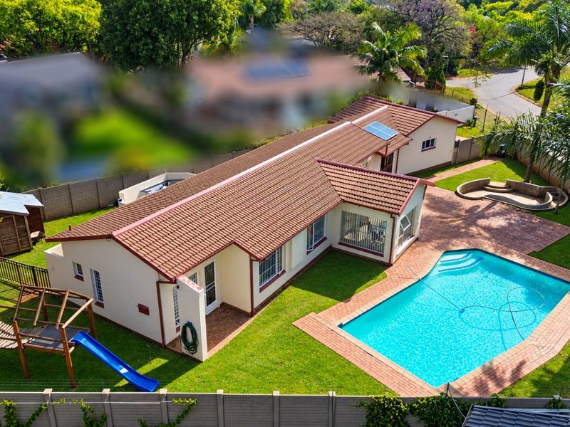 Aerial view of a residential property featuring a tiled roof, swimming pool, paved patio area, and a well-maintained garden.