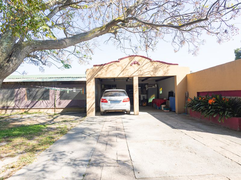 Front view of the property featuring a double garage, concrete driveway, and a covered patio area with established garden elements.