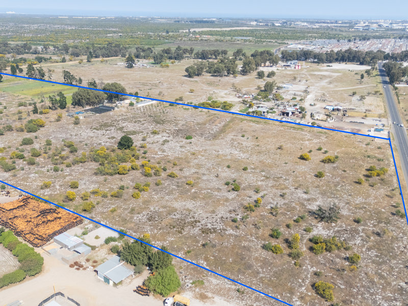 Aerial view of a large, undeveloped small holding plot with clear boundary lines, situated adjacent to a main road.