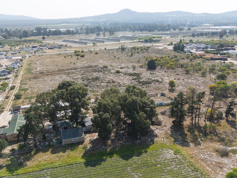 Aerial view of a small holding property featuring cultivated land, mature trees, and multiple outbuildings set within a rural landscape.