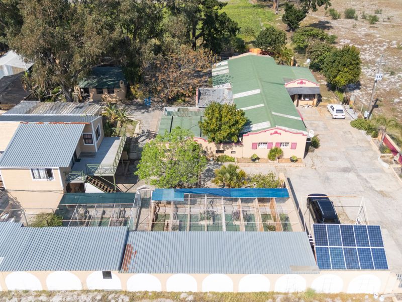 Aerial view of the small holding property featuring multiple outbuildings, corrugated metal roofing, solar panels, and extensive fenced outdoor areas.