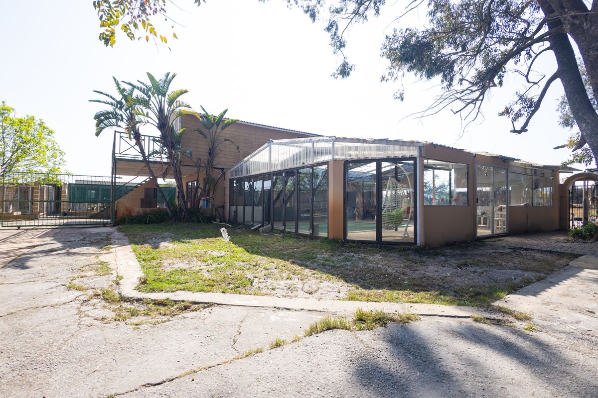 Rear view of the property featuring an enclosed patio structure, concrete driveway, and an elevated balcony area on a small holding.
