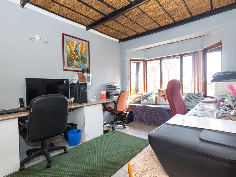 A functional home office featuring a built-in desk, a large bay window for natural light, and a unique thatched ceiling finish.