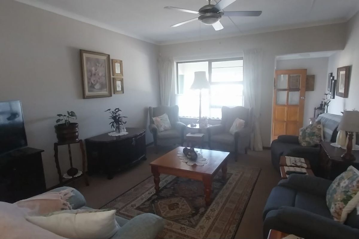 A comfortable living room featuring carpeted flooring, a ceiling fan, and natural light through a large window.