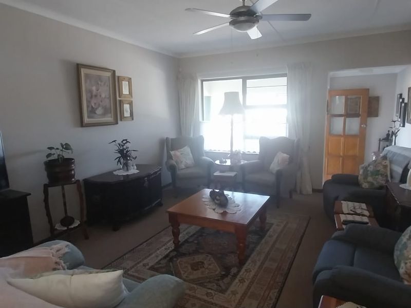 A comfortable living room featuring carpeted flooring, a ceiling fan, and natural light through a large window.