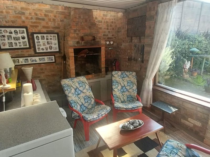 Covered patio area featuring an exposed brick finish, a built-in brick braai, and large windows overlooking the rear garden.