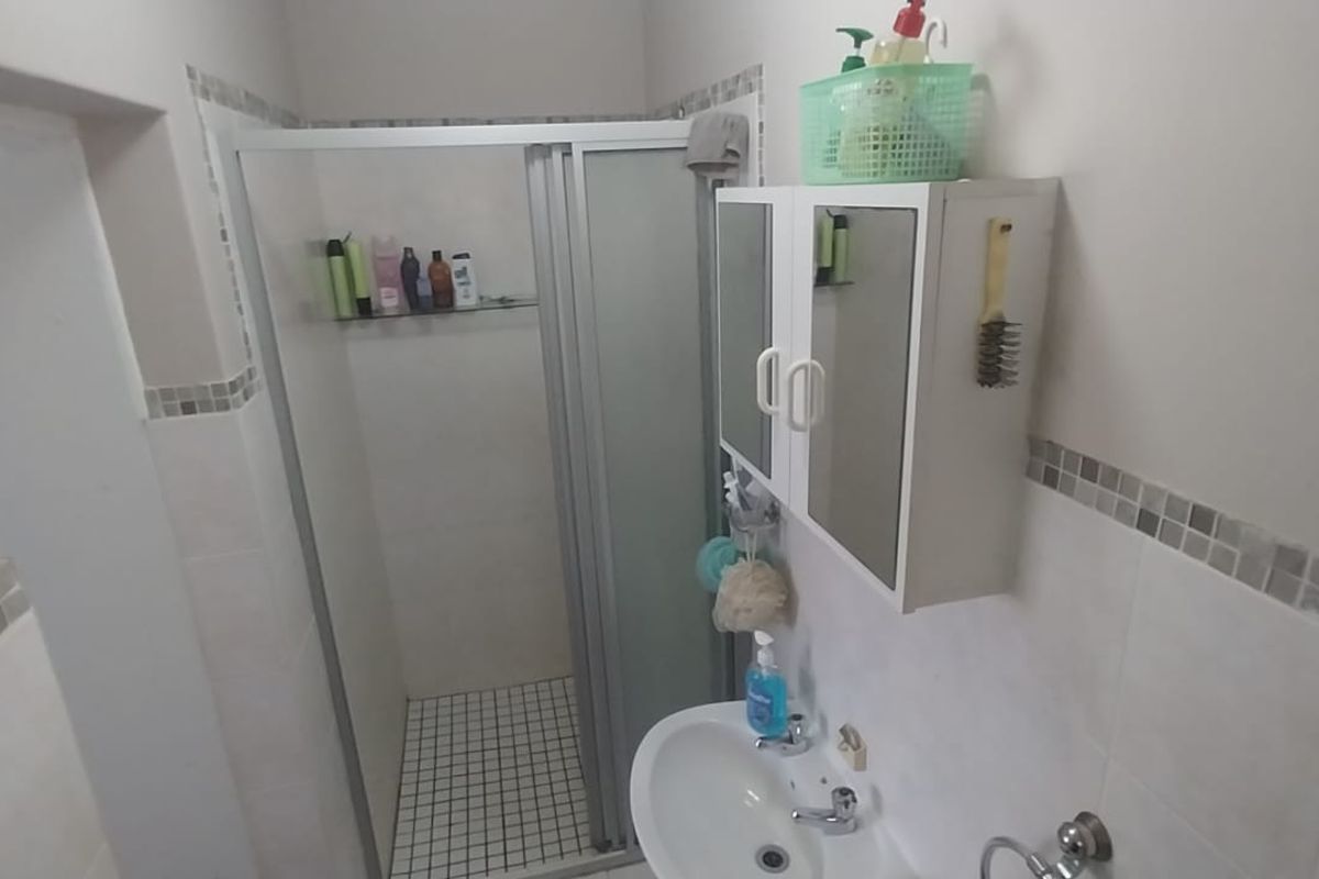 A functional bathroom featuring a shower enclosure, pedestal basin, and wall-mounted medicine cabinet with decorative mosaic tile accents.