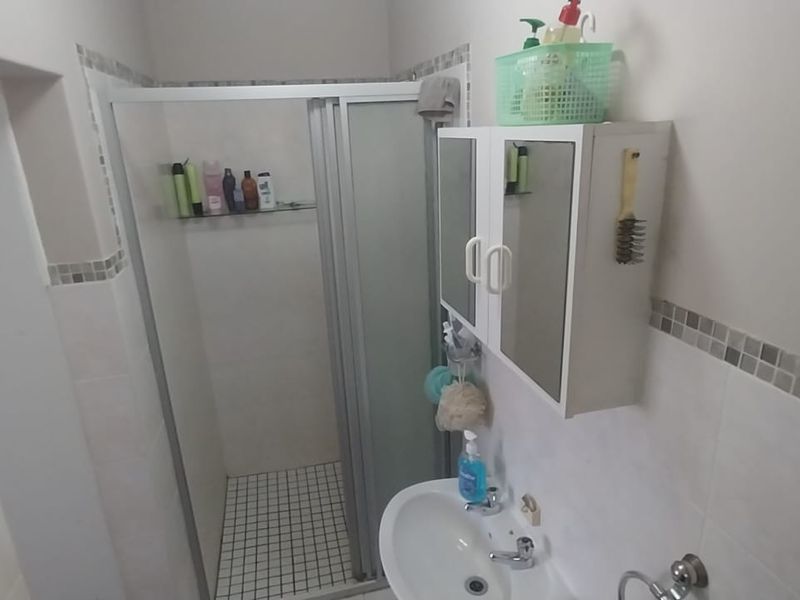 A functional bathroom featuring a shower enclosure, pedestal basin, and wall-mounted medicine cabinet with decorative mosaic tile accents.