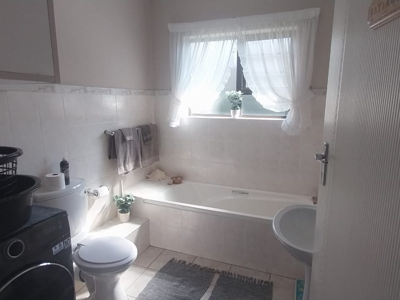 A functional bathroom featuring a bathtub, pedestal basin, and toilet with tiled finishes and natural light from a window.