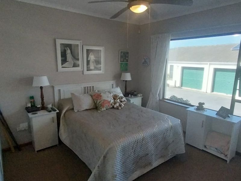 A functional bedroom featuring a ceiling fan, built-in cupboards, and large aluminium-framed windows providing natural light.