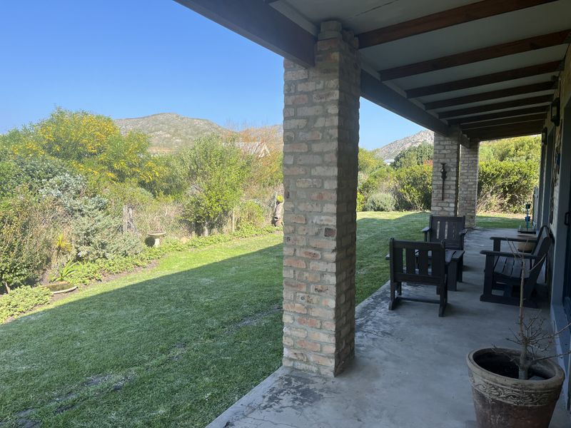 A covered patio featuring exposed timber beams and brick columns, overlooking a lush garden with mountain views.