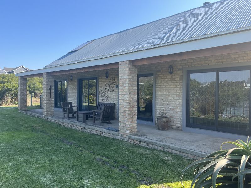 A spacious covered patio featuring exposed brick pillars, concrete flooring, and multiple sliding glass doors providing seamless access to the garden.