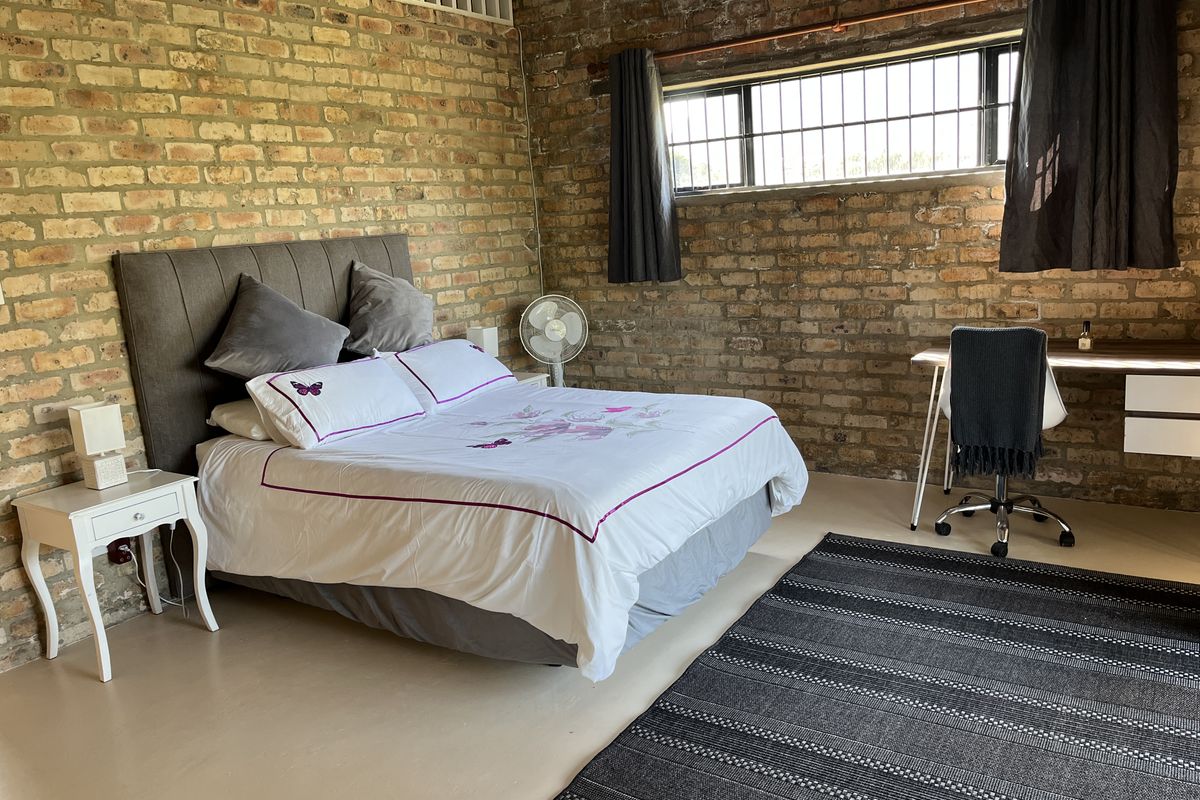 Spacious bedroom featuring industrial-style exposed brick walls, polished concrete flooring, and a high-set horizontal window with security bars.