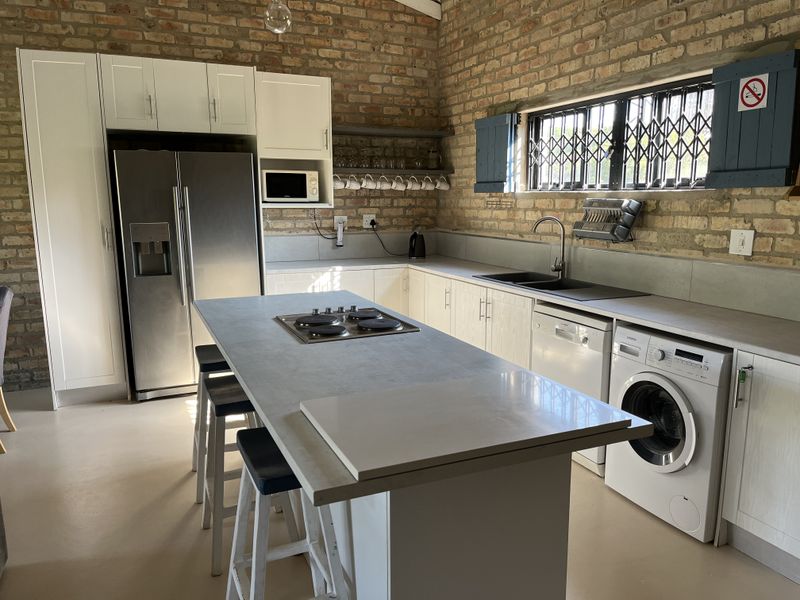 Modern kitchen featuring exposed brick walls, a central island with a built-in hob, integrated appliances, and ample cabinetry, offering a stylish industrial aesthetic.