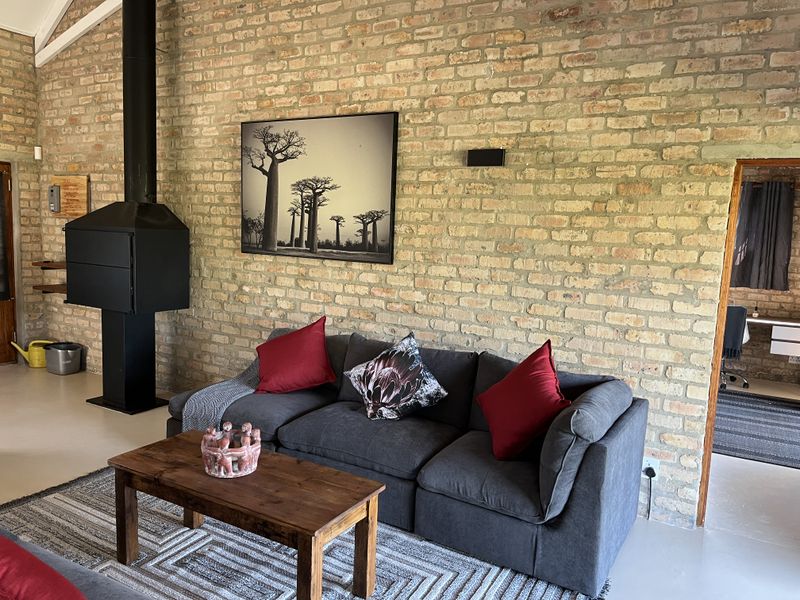 A cozy living room featuring a striking exposed brick wall, a modern freestanding fireplace, and a high vaulted ceiling.
