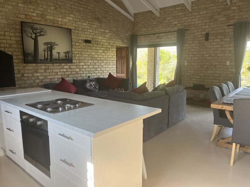 Spacious open-plan living area featuring exposed brick walls, a vaulted ceiling, and a modern kitchen island with built-in appliances, leading to outdoor access.